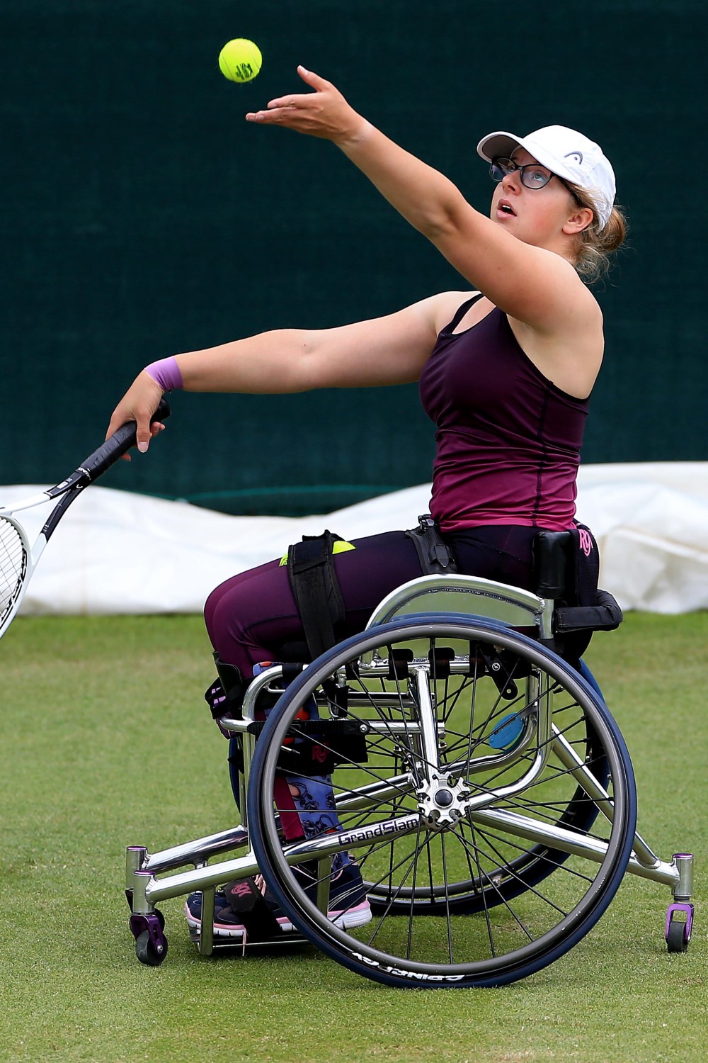 Abbie Breakwell on court in her wheelchair throwing a ball in the air to hit a serve