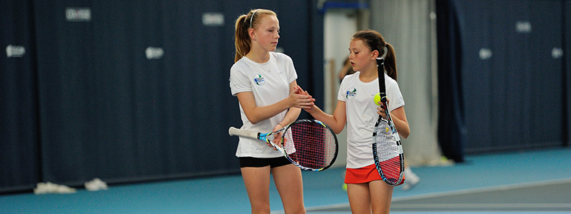 Two girls high five on a tennis court