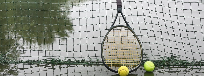A tennis racket and set of tennis balls on a rainy tennis court